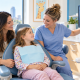 Children'S Dental X-Rays: Questions Parents Can Ask At A Checkup 3 A Dental Professional In Blue Scrubs Points To A Panoramic Dental X-Ray On A Wall Monitor While A Smiling Young Girl In A Dental Bib Reclines In A Blue Chair Beside Her Caregiver.